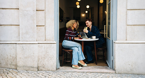 Friends sharing laptop at a sunny outdoor cafe