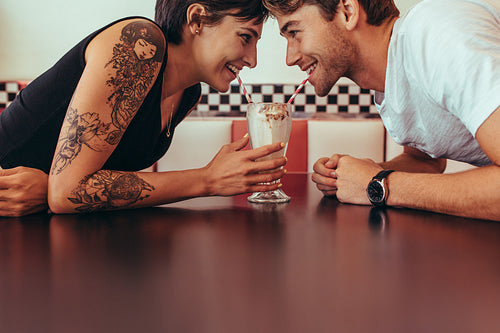 Man and woman sharing milk shake from one glass using straws