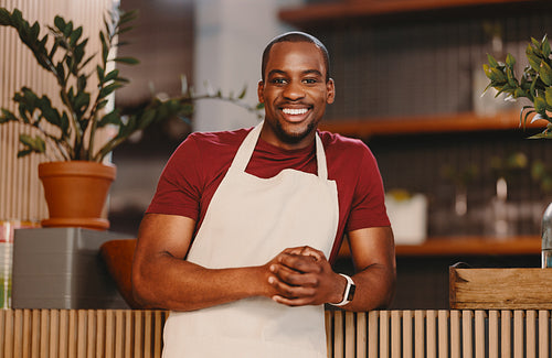 Cheerful entrepreneur standing in an apron, ready to serve customers at a cafe