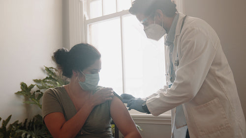 Doctor inoculating a female patient with the covid-19 shot in her home