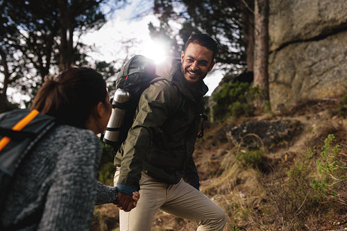 Hiker helping his girlfriend uphill on country path.