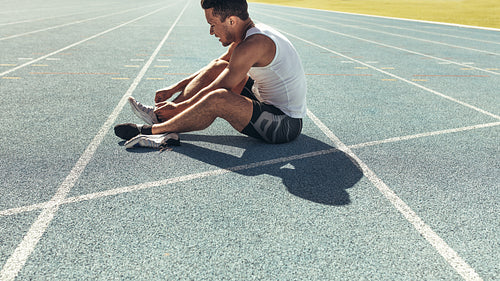 Sprinter tying shoe lace sitting on running track