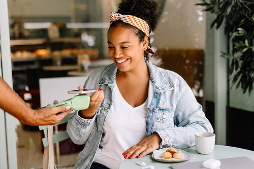 Cheerful woman using NFC with her phone to make a payment at cafe