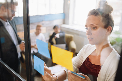 Business woman looking at adhesive notes in conference room