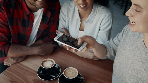 Woman with friends taking photos of coffee at cafe