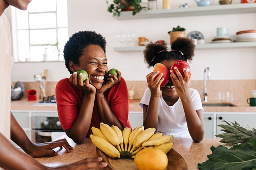 Mother and daughter, happy and playful at home with fresh fruits