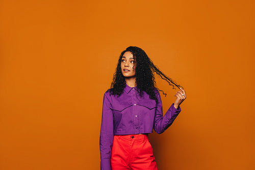 Thoughtful woman with curly hair standing on vibrant orange background