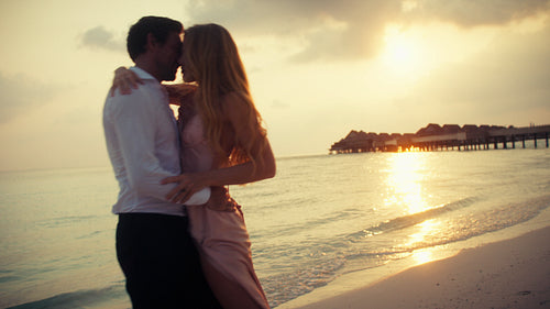 A romantic couple embraces on a luxurious tropical beach during a stunning sunset