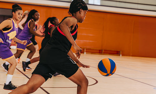 Group of teenage girls playing competitive basketball on a hardwood court