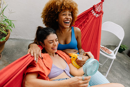 Two women relaxing and laughing in a hammock on a sunny day