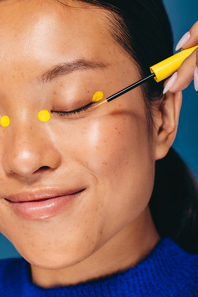 Applying eyeliner dots with a brush, young female does her makeup in a studio