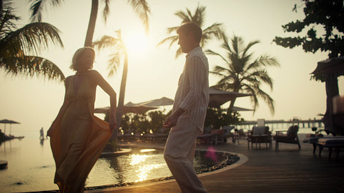 Mature couple dancing gracefully by the pool at a tropical resort during sunset