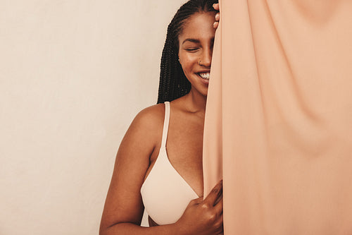 Beautiful young woman smiling behind a studio curtain