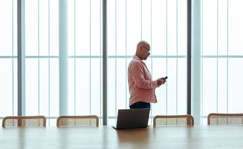 Caucasian businessman in a modern boardroom using a smartphone with a laptop on the table