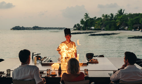 Chef prepares teppanyaki at a beachfront restaurant with an audience