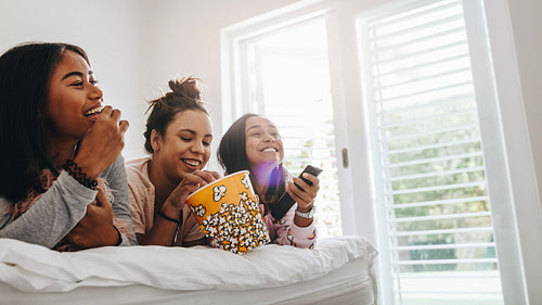 Girls watching television lying on bed eating popcorns