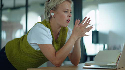 Focused woman talks and types on a laptop during an online meeting at a desk