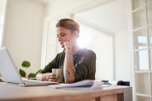 Young woman with coffee looking at laptop