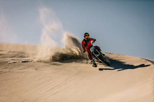 Motocross rider riding over sand dunes