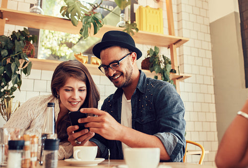 Friends looking at mobile phone while sitting in cafe