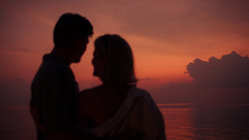 A loving couple embraces intimately against a vibrant sunset backdrop
