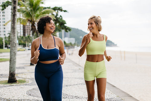 Two women jogging on beach promenade, embracing a fit lifestyle during summer