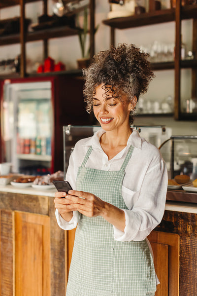 Mature cafe owner using a smartphone in her shop