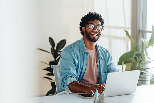 Happy business man working with a laptop in an office with potted plants