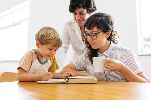 Female couple looking at their son scribbling in a book