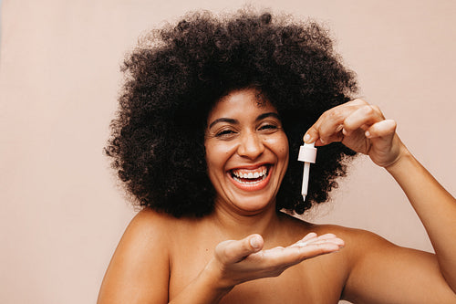 Cheerful young woman dropping face serum onto her palm