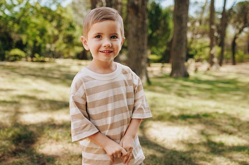 Smiling young boy in a striped shirt enjoying a sunny day outdoors