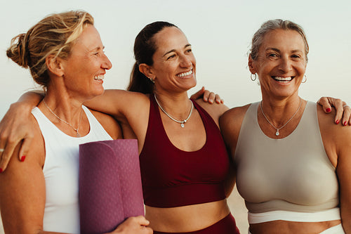 Happy mature women embracing and smiling outdoors in yoga attire