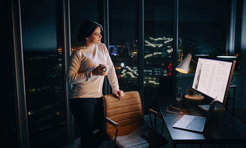 Thoughtful business woman looking at her computer screen while working late in her office