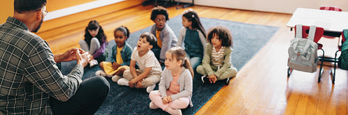 Teaching a primary school class. Male educator sits in front of little students