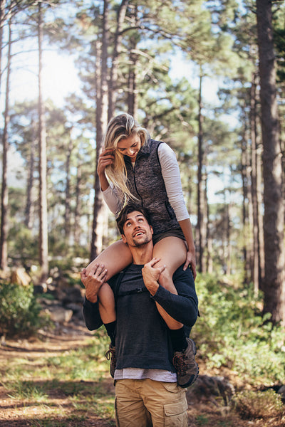 Man carrying his woman partner on his shoulders while trekking in forest 