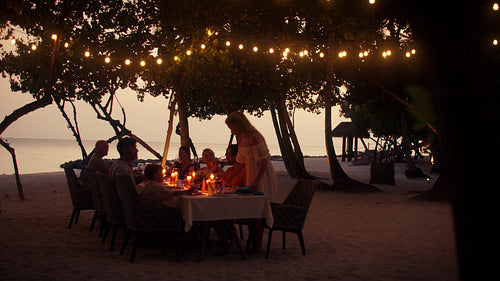 Family enjoys an unforgettable and intimate candlelit dinner on a beautiful island beach at sunset