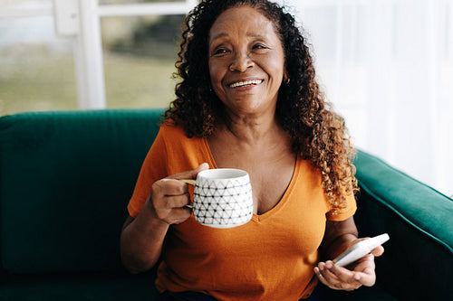 Elderly woman holding a smartphone as she enjoys a warm cup of coffee