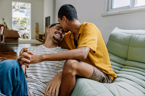 Gay couple laughing and embracing in a cozy living room