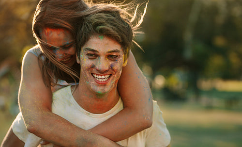 Smiling woman piggy riding on a man while playing holi in a park
