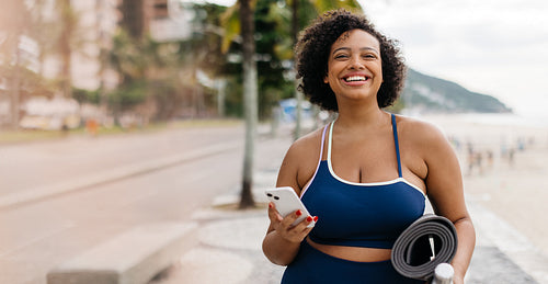 Fitness at the beach: Woman smiling and going for a workout with her phone in hand