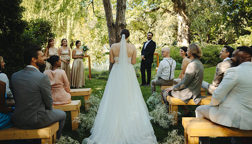 Outdoor wedding ceremony with bride, guests, and bridesmaids in lush garden setting