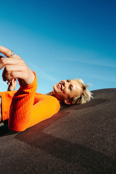 Playful woman in orange top poses on urban slope under blue sky