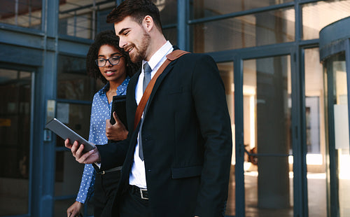 Business colleagues with digital tablet walking out of office