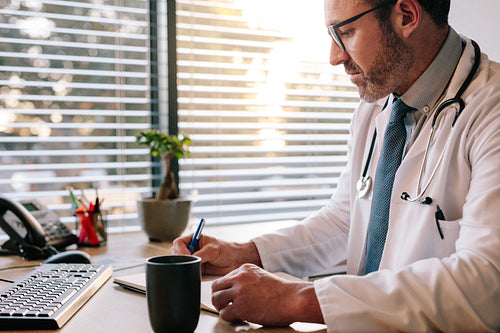 Doctor at office making notes in his diary