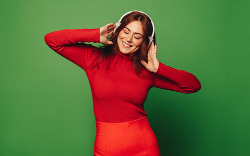 Young woman smiling and enjoying music with wireless headphones on a green background