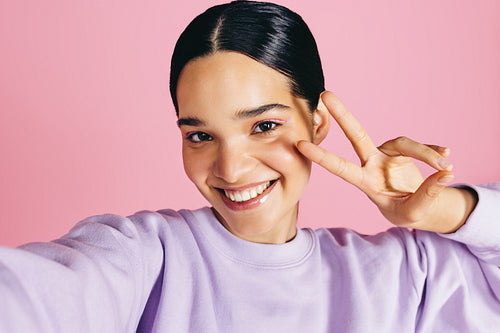 Woman taking a selfie in a studio, smiling at the camera and doing a peace sign