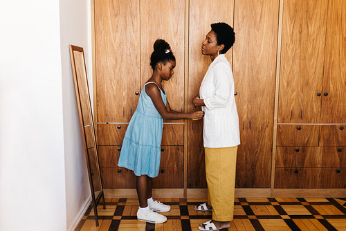 Caring little girl helping her mom get dressed in front of the mirror, buttoning her jacket