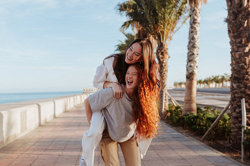 Vibrant young woman piggybacking her best friend in the promenad