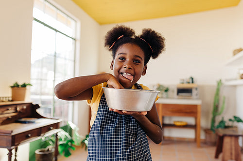 Happy girl tasting cake dough from a bowl, enjoying baking time at home