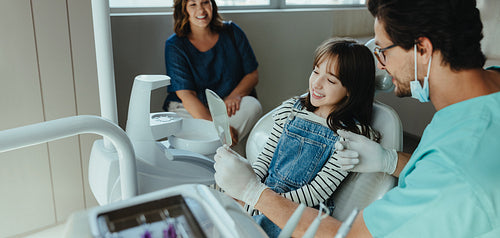 A Dentist shows the child her smile during a family dental visit with a hand mirror